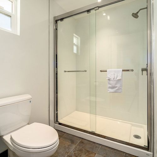 The image shows a bathroom with a toilet and a glass-enclosed shower. A towel is hanging on the shower door handle.