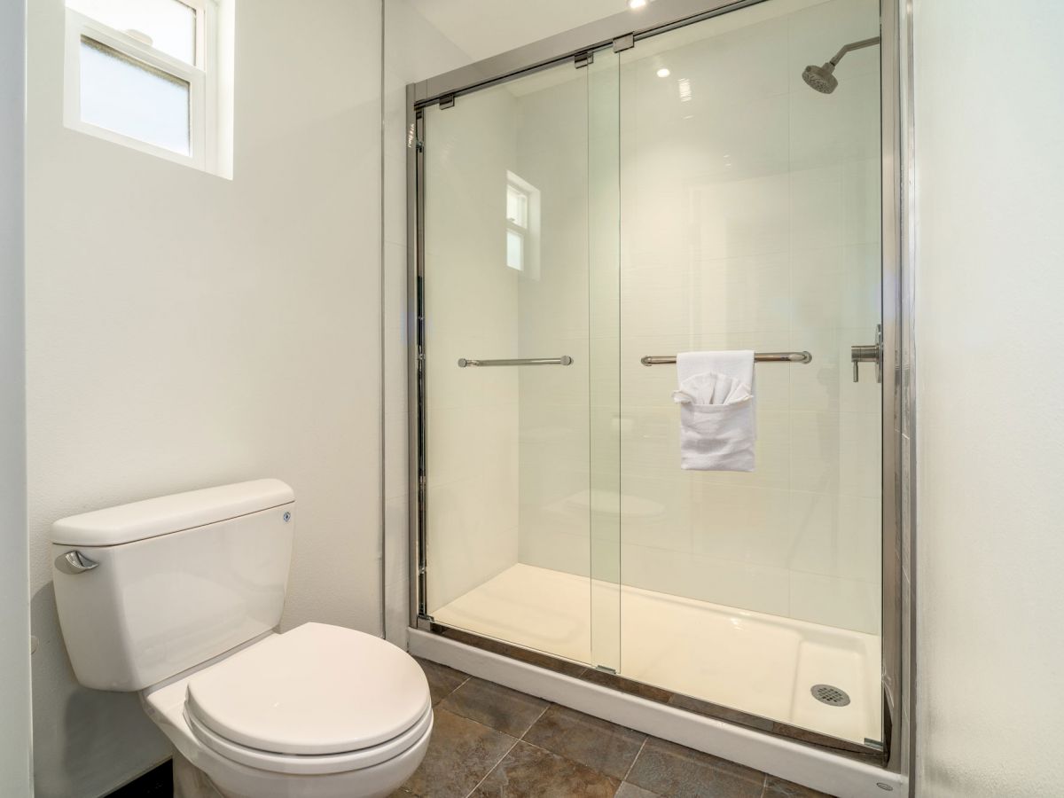 A clean, minimalist bathroom with a toilet and a glass-enclosed shower stall, featuring a white towel hanging on the shower door handle.