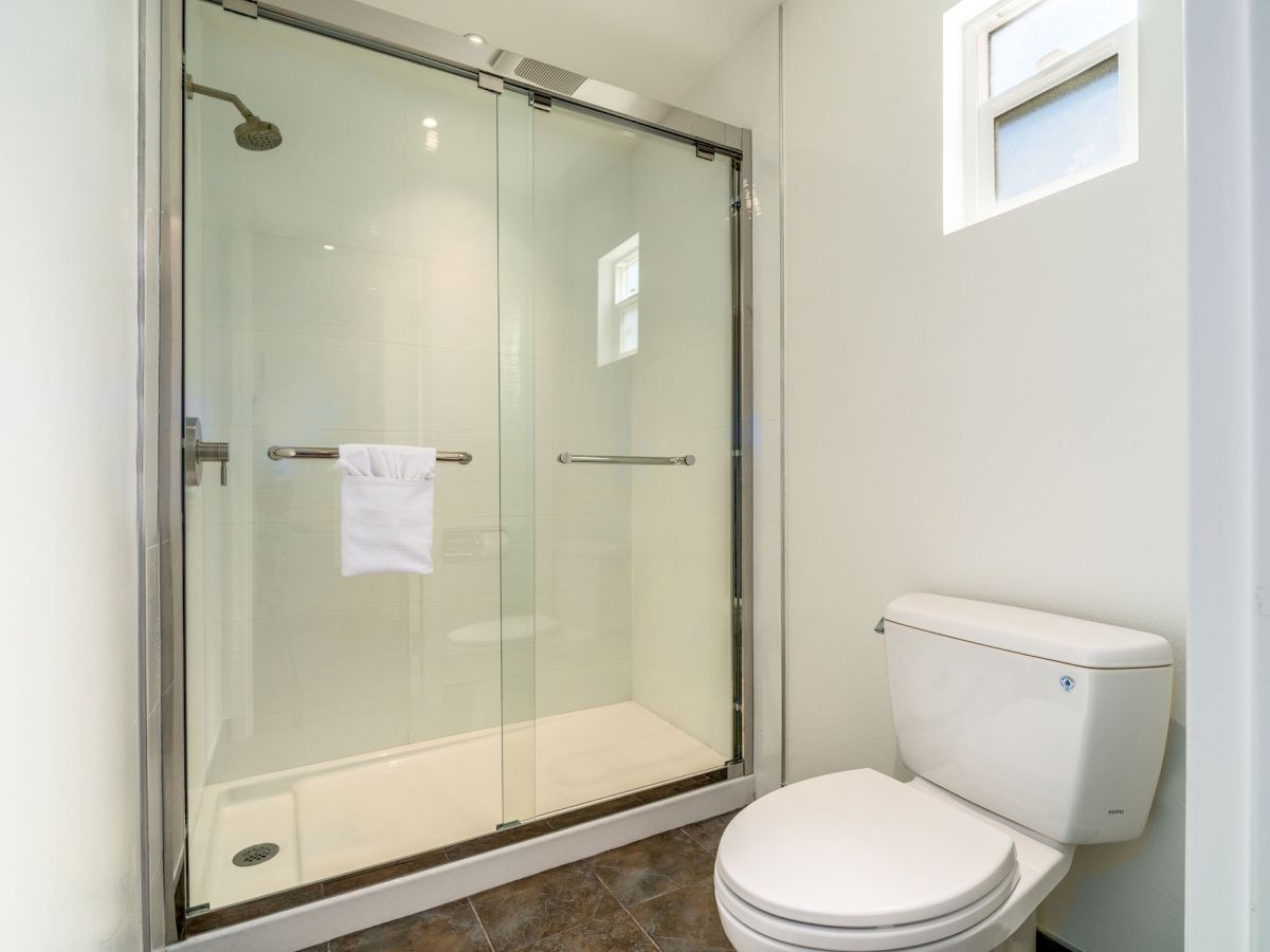 A clean bathroom with a glass-enclosed shower, a white towel hanging, a white toilet, and a small window on a white wall.