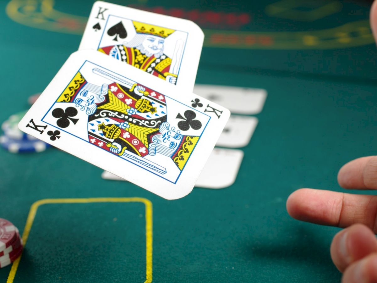 A person is flipping playing cards on a green felt table, with gambling chips nearby. The visible cards are the king of spades and the king of clubs.