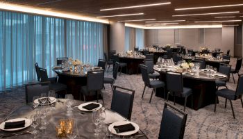 A banquet hall is set up with round tables covered in black tablecloths, elegant table settings, and black napkins, with floral centerpieces and candles.
