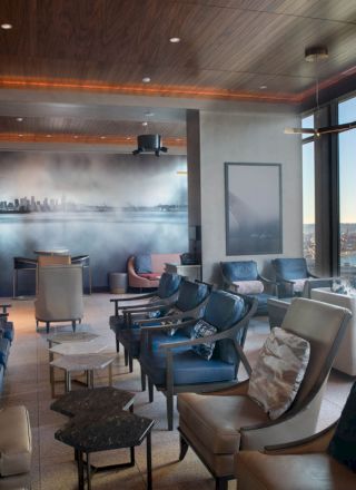 This image shows a modern lounge area with comfortable seating, large windows offering a scenic view, and a cityscape mural on the wall.