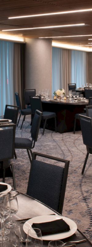 A stylish dining area with multiple round tables covered in fine dinnerware, black napkins, elegant centerpieces, and chairs on a patterned carpet.