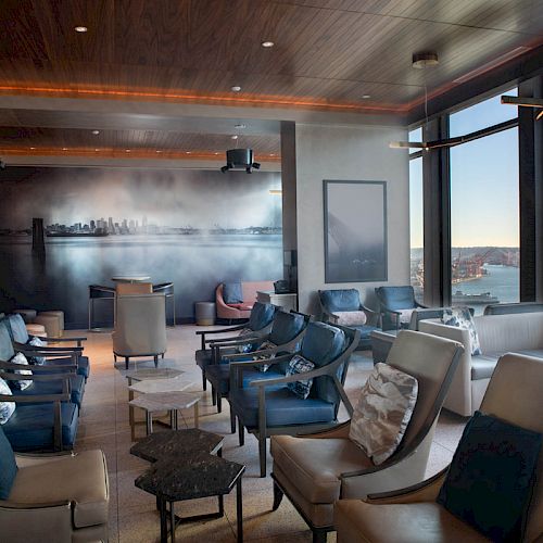 A modern lounge with plush seating, large windows offering a scenic view, and a mural on the back wall, with a relaxed, inviting atmosphere.