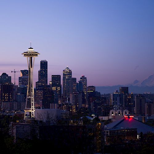 The image shows a twilight cityscape of Seattle, featuring the Space Needle prominently with Mount Rainier visible in the background.